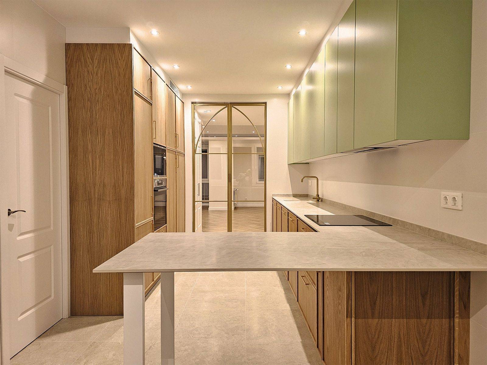 Península de encimera gris claro sobre patas blancas, con la cocina de madera y verde detrás