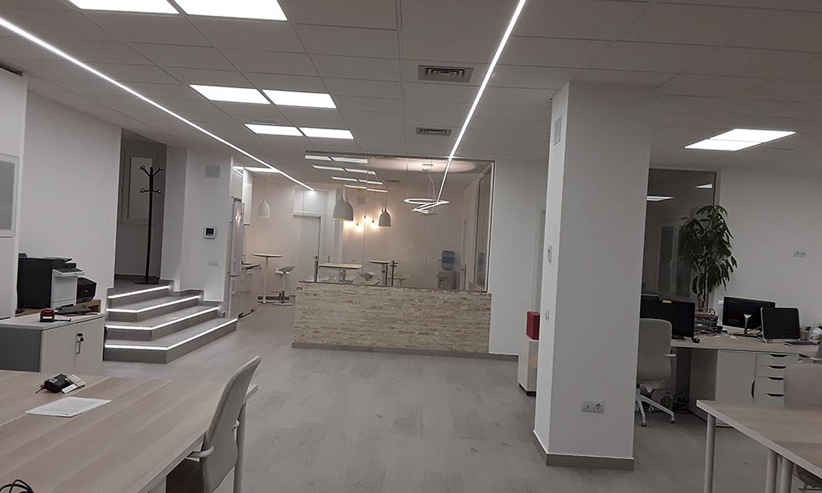 Oficina diáfana terminada, con puestos de trabajo, techo con tiras LED y la escalera iluminada al fondo