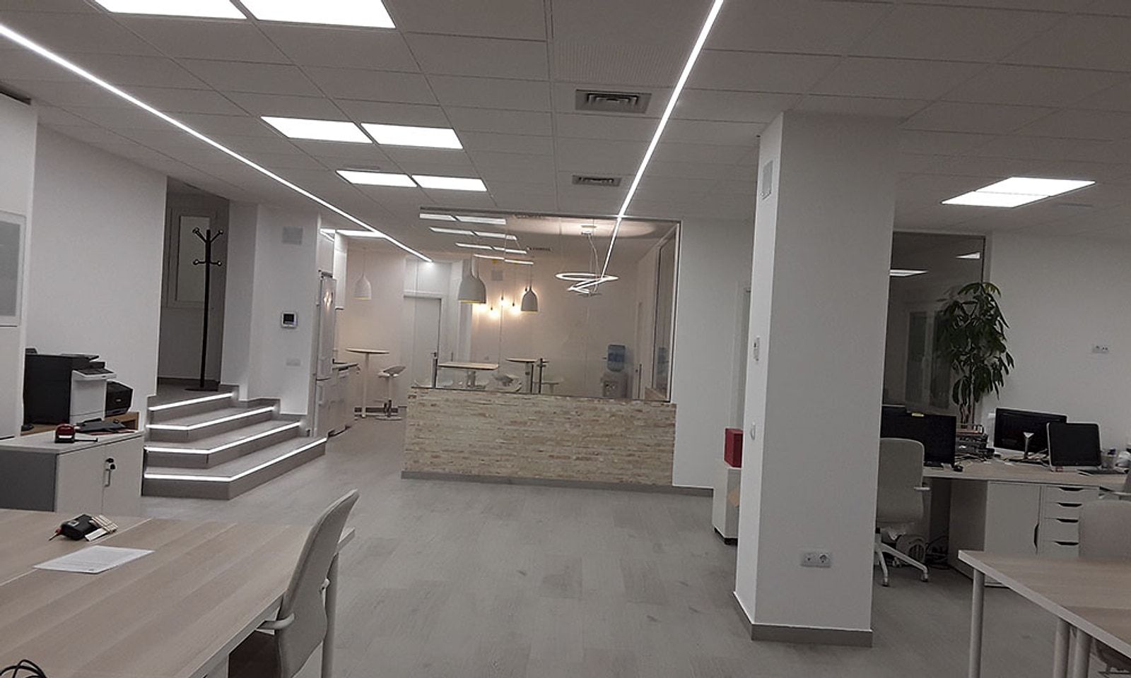 Oficina diáfana terminada, con puestos de trabajo, techo con tiras LED y la escalera iluminada al fondo