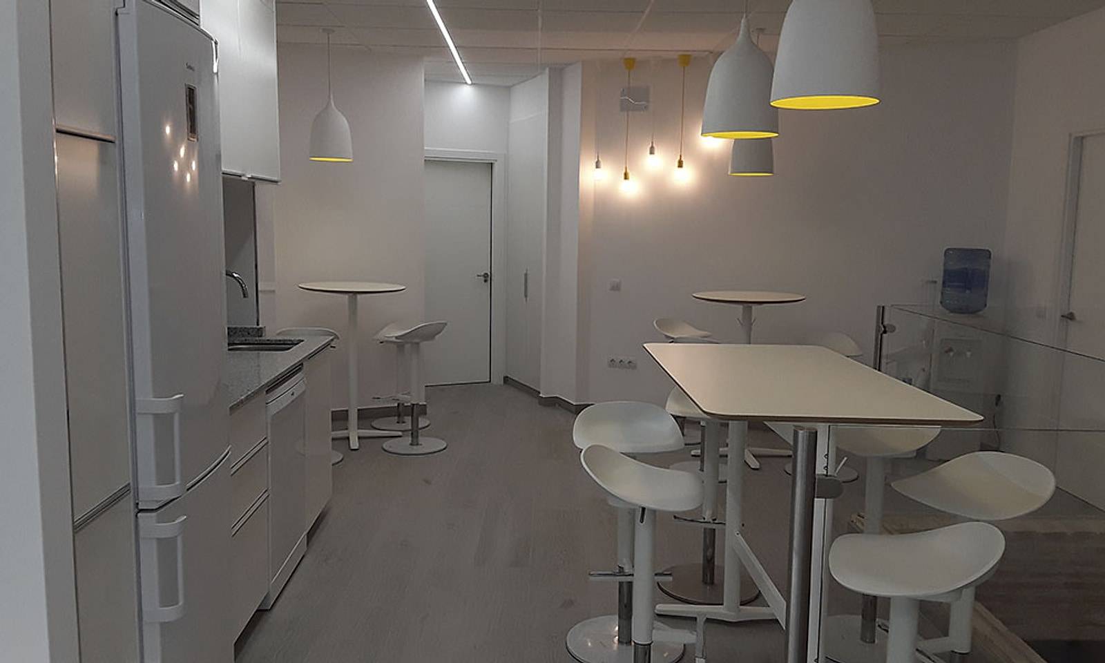 Office con mesas altas y taburetes blancos, cocina y lámparas colgantes