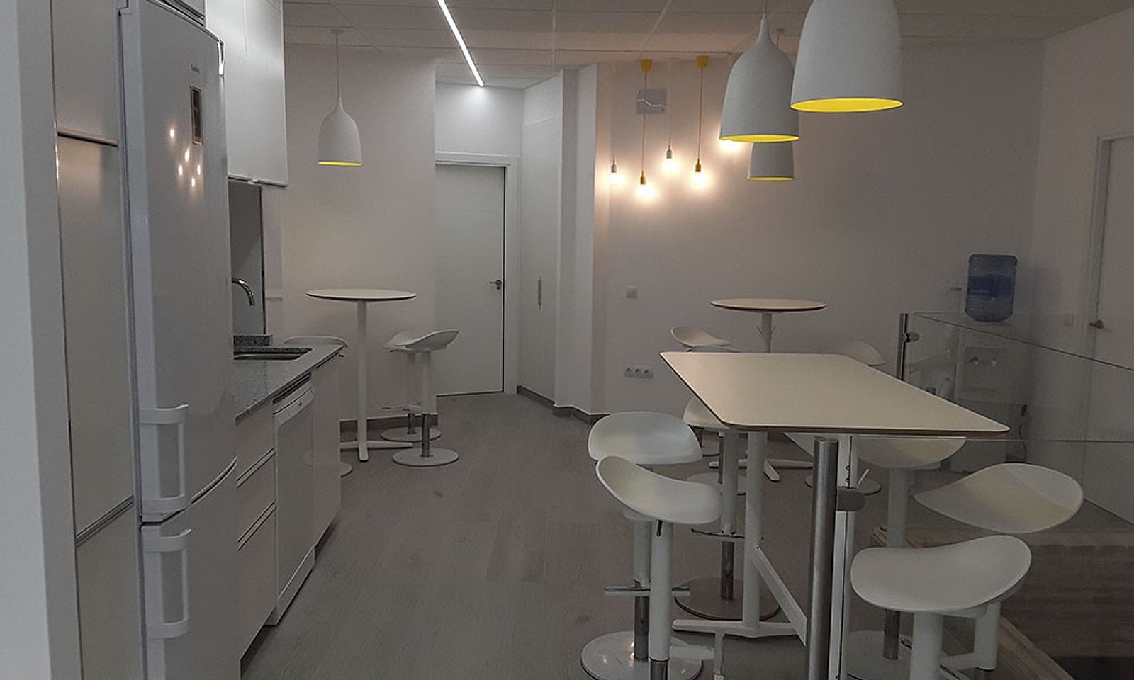 Office con mesas altas y taburetes blancos, cocina y lámparas colgantes