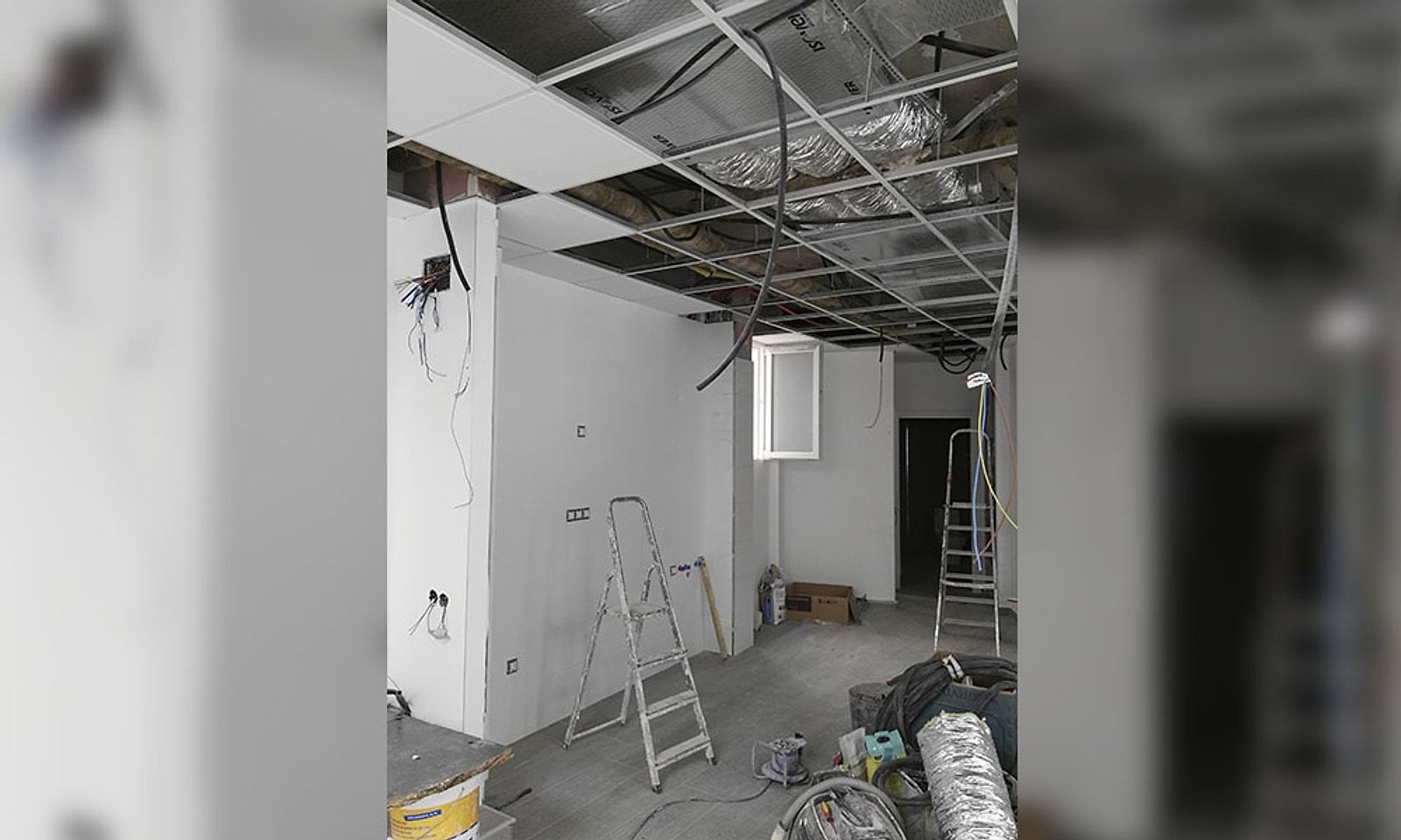 Zona de una oficina en obra, con el falso techo desmontado y los conductos a la vista