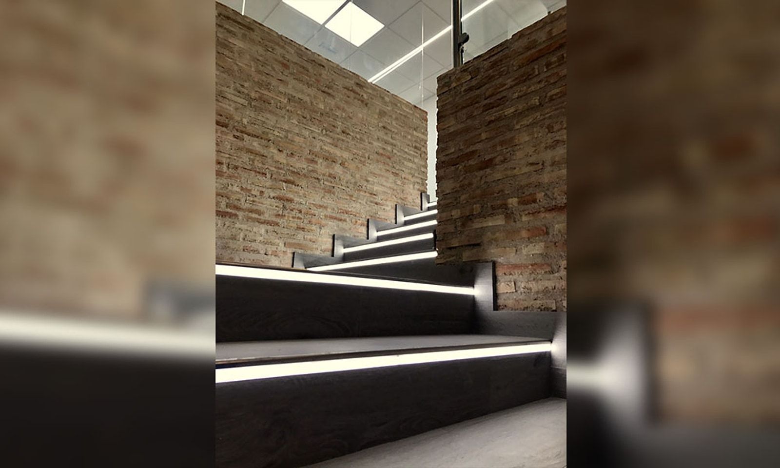 La misma escalera terminada, con pared de ladrillo rústico y tiras de luz en cada peldaño
