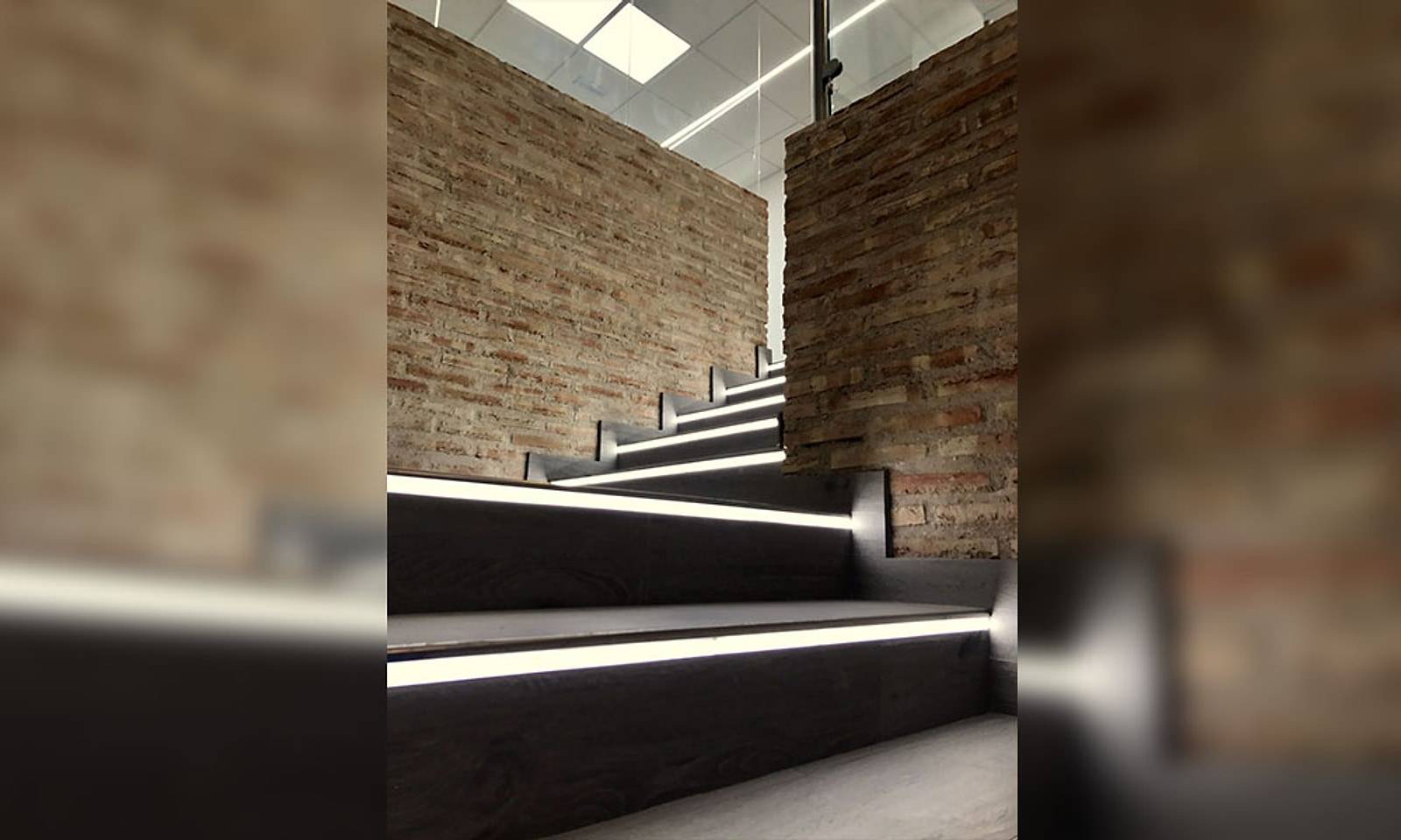 La misma escalera terminada, con pared de ladrillo rústico y tiras de luz en cada peldaño