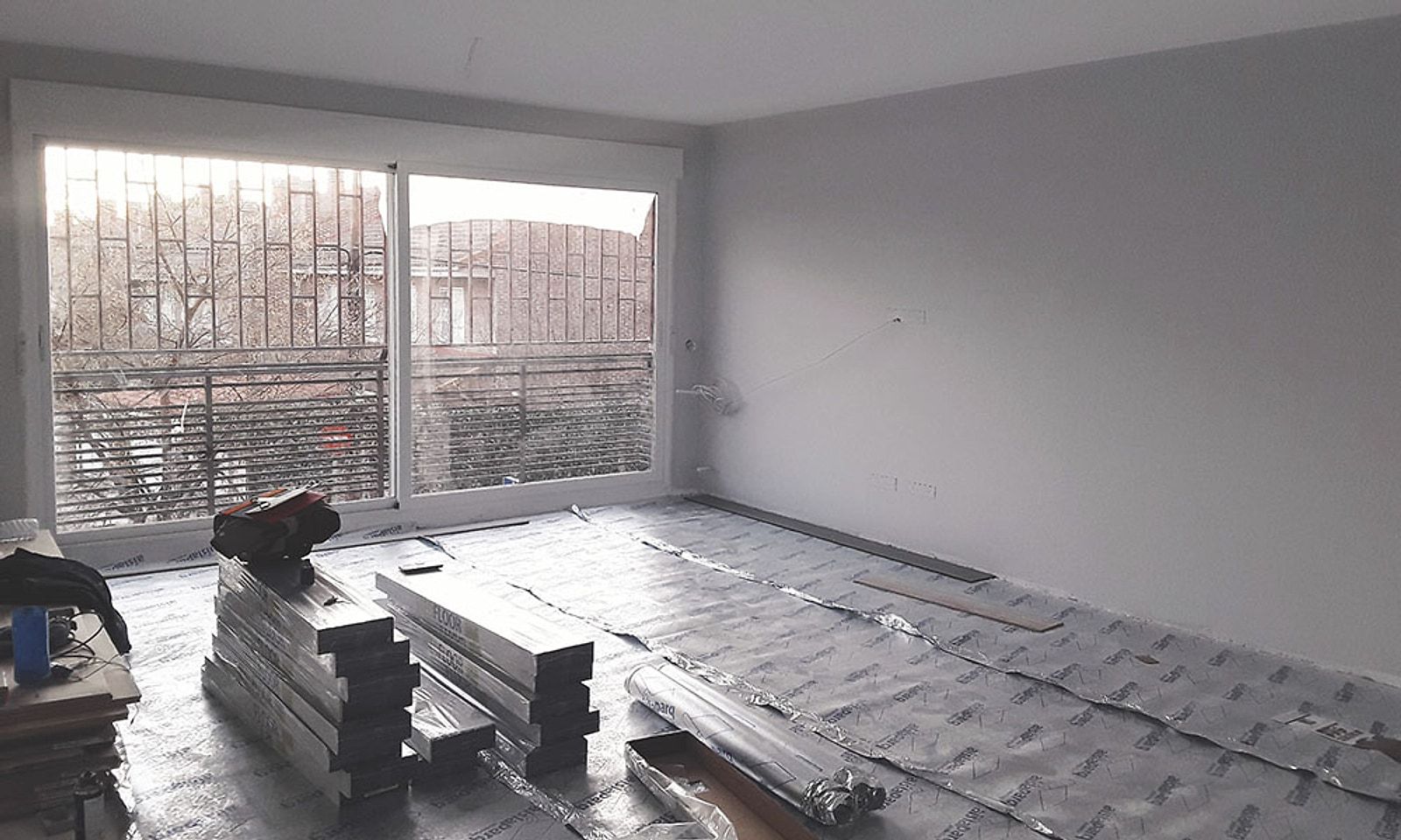 Salón del piso durante la obra, con la lámina aislante en el suelo y las cajas de tarima apiladas