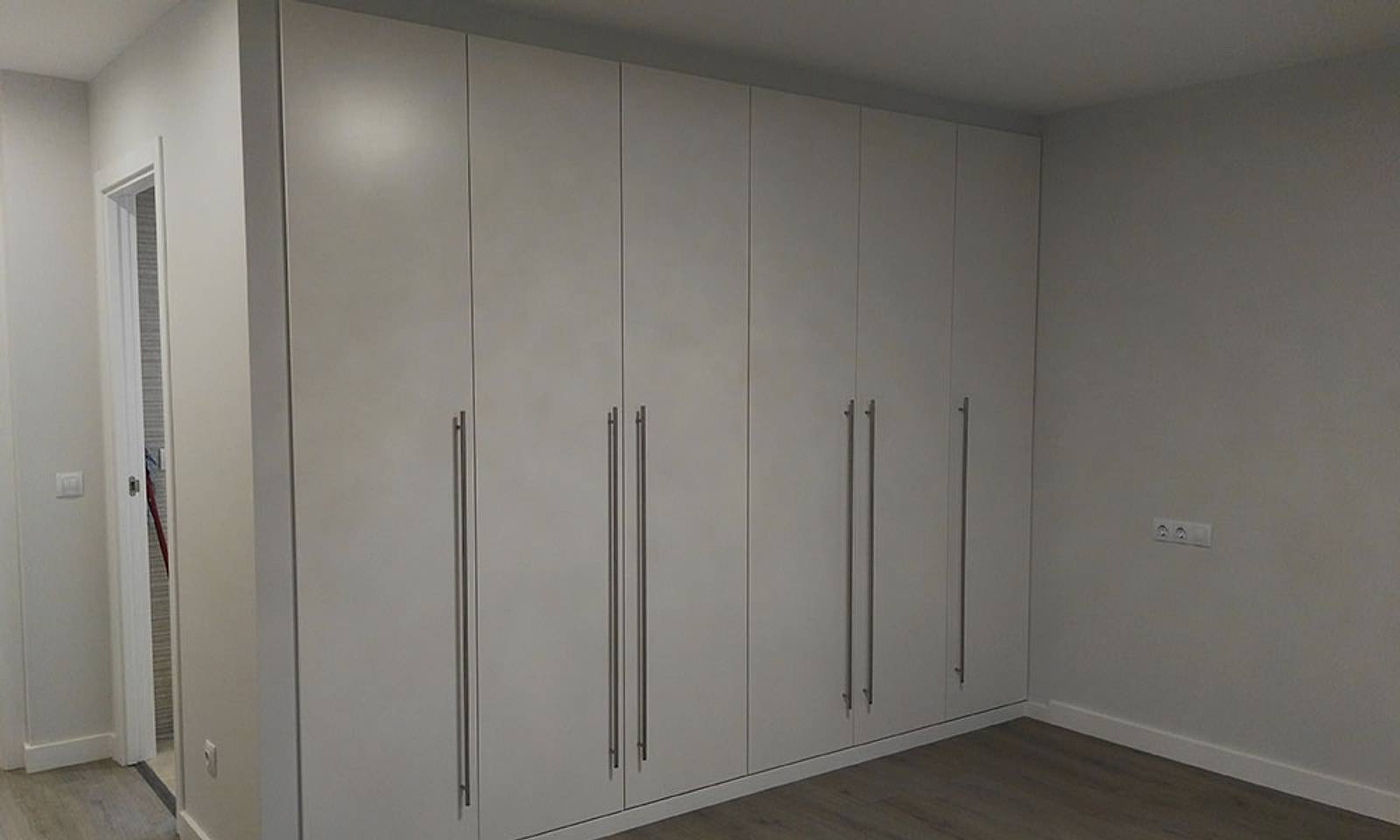 Dormitorio con una pared entera de armarios empotrados blancos