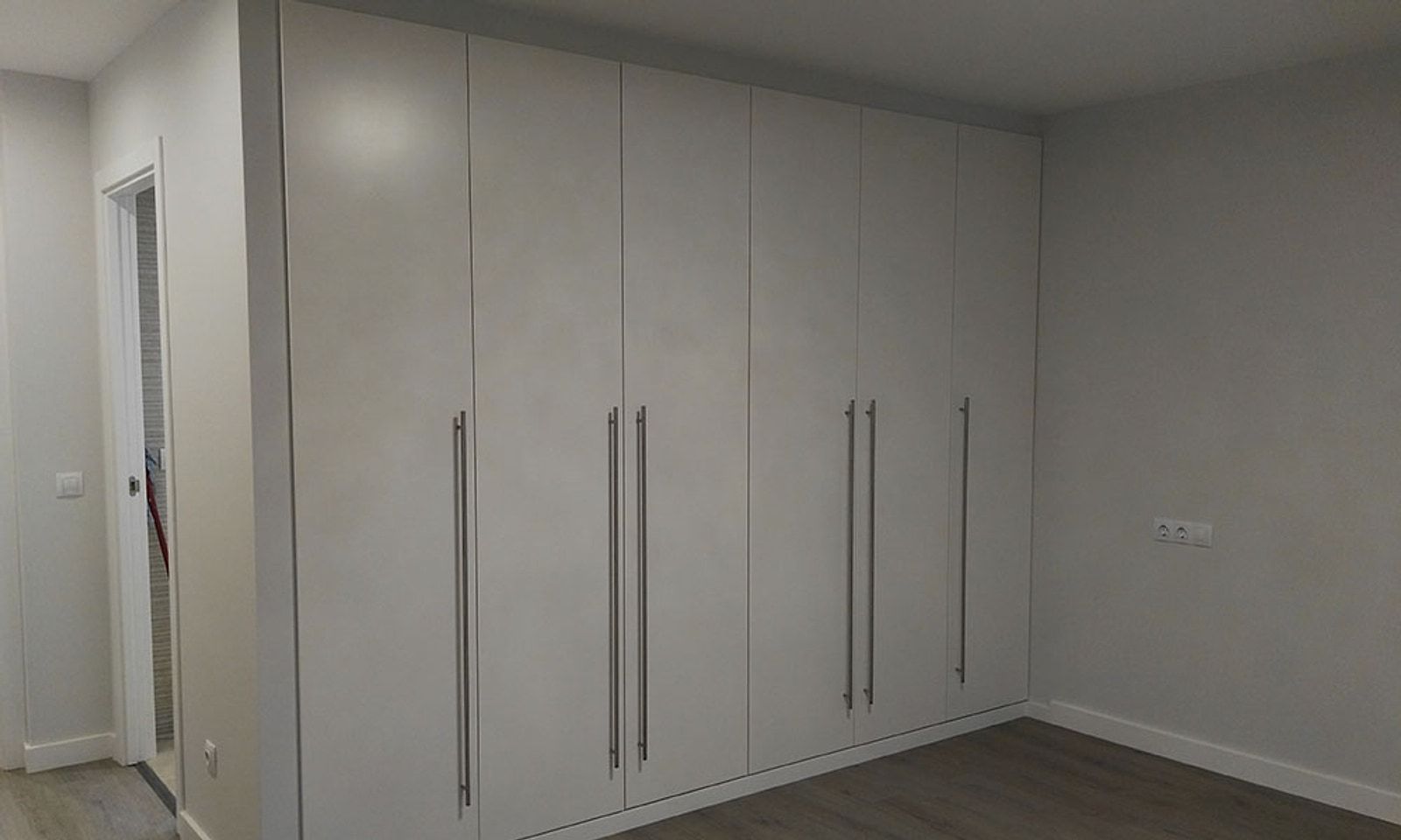 Dormitorio con una pared entera de armarios empotrados blancos