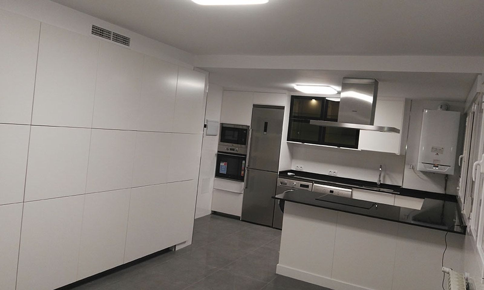 Cocina del piso con muebles blancos sin tiradores, encimera negra y electrodomésticos en torre