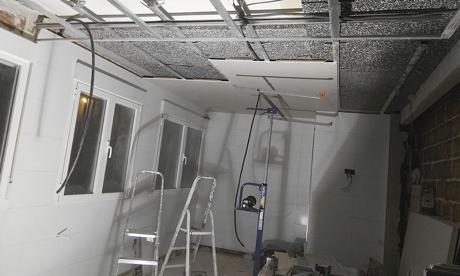 Cocina de un piso en obra, con el falso techo abierto y escaleras de pintor