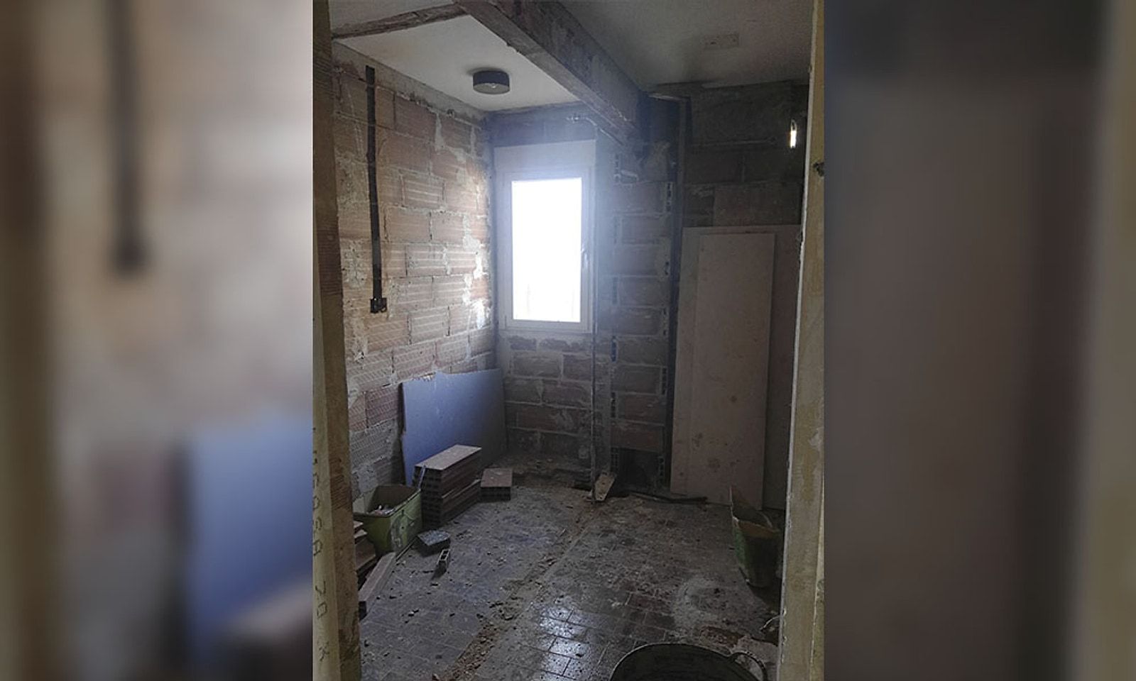 Baño de un piso en obra, con las paredes de ladrillo a la vista y escombro en el suelo