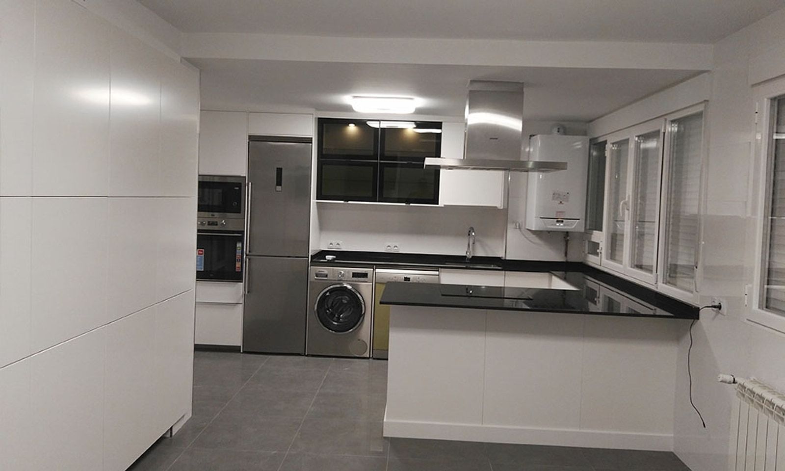 Cocina del piso terminada, blanca, con encimera negra y electrodomésticos en torre