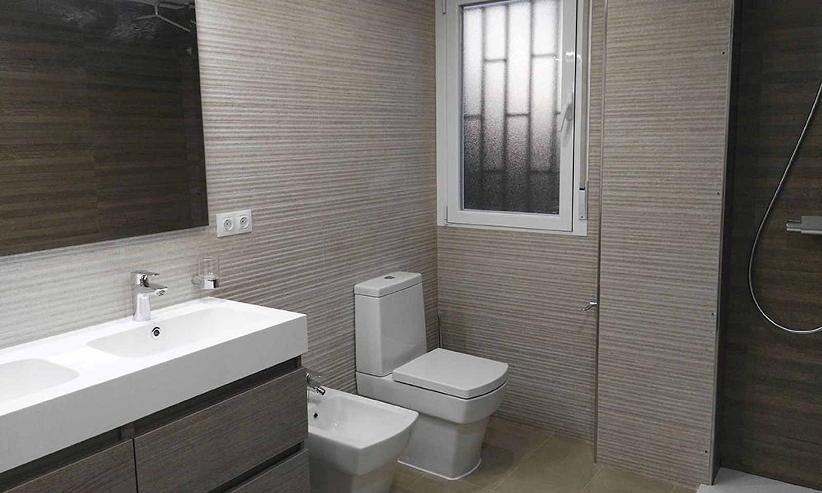 El mismo baño terminado, con mueble de lavabo, inodoro y bidé nuevos junto a la ventana