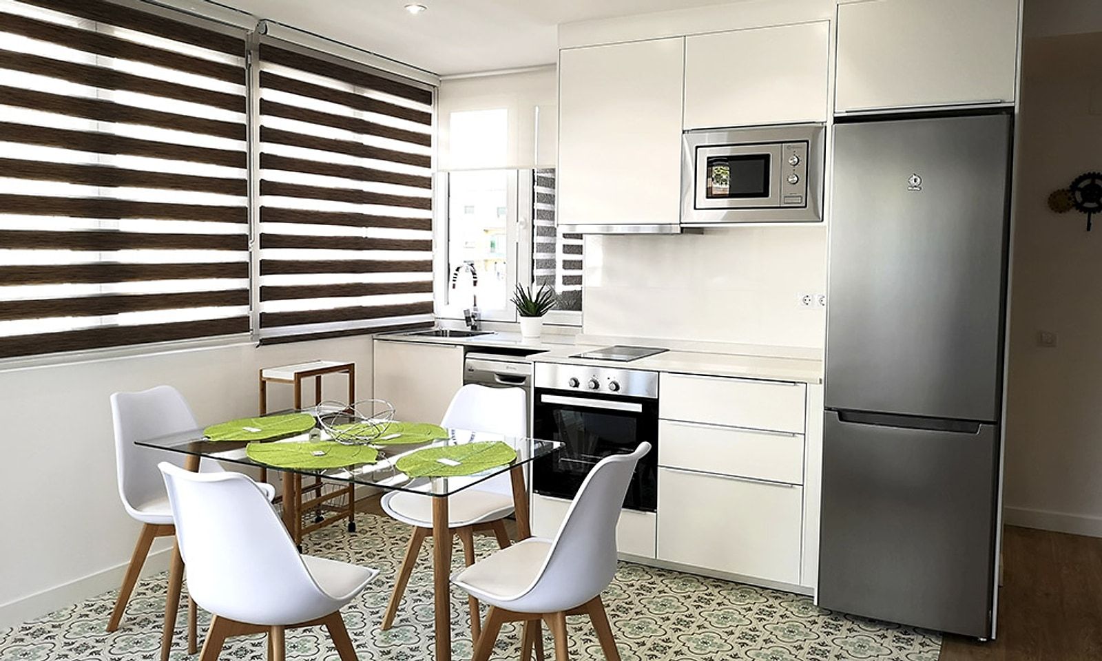 Cocina blanca con alicatado claro, frigorífico de acero y mesa de comedor con sillas blancas