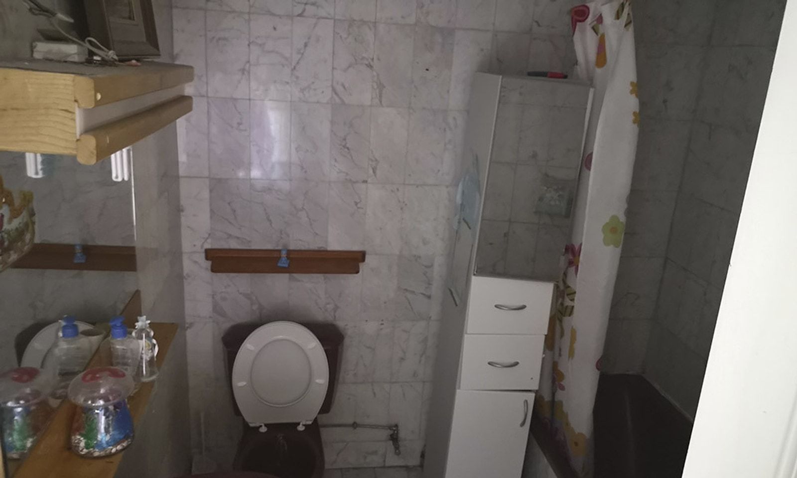 Baño antiguo con azulejo de mármol, bañera y muebles viejos