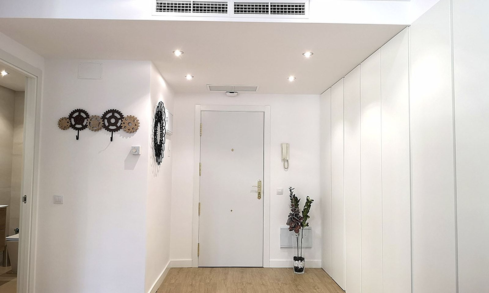 Entrada del piso terminada, blanca, con armario empotrado y rejillas de aire en el techo