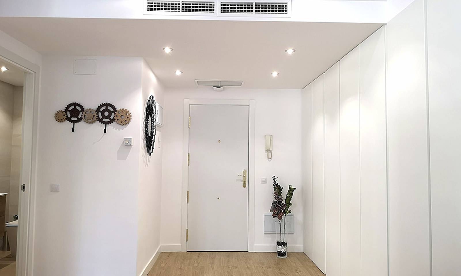 Entrada del piso terminada, blanca, con armario empotrado y rejillas de aire en el techo