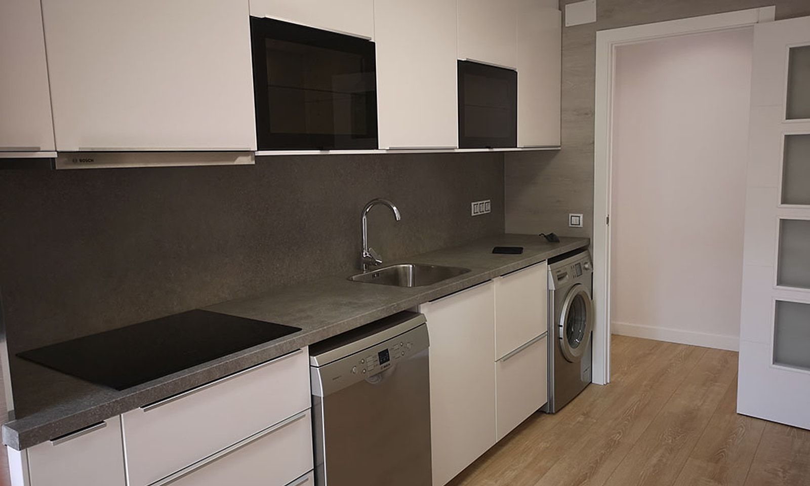 Cocina con placa de inducción, encimera gris y muebles blancos