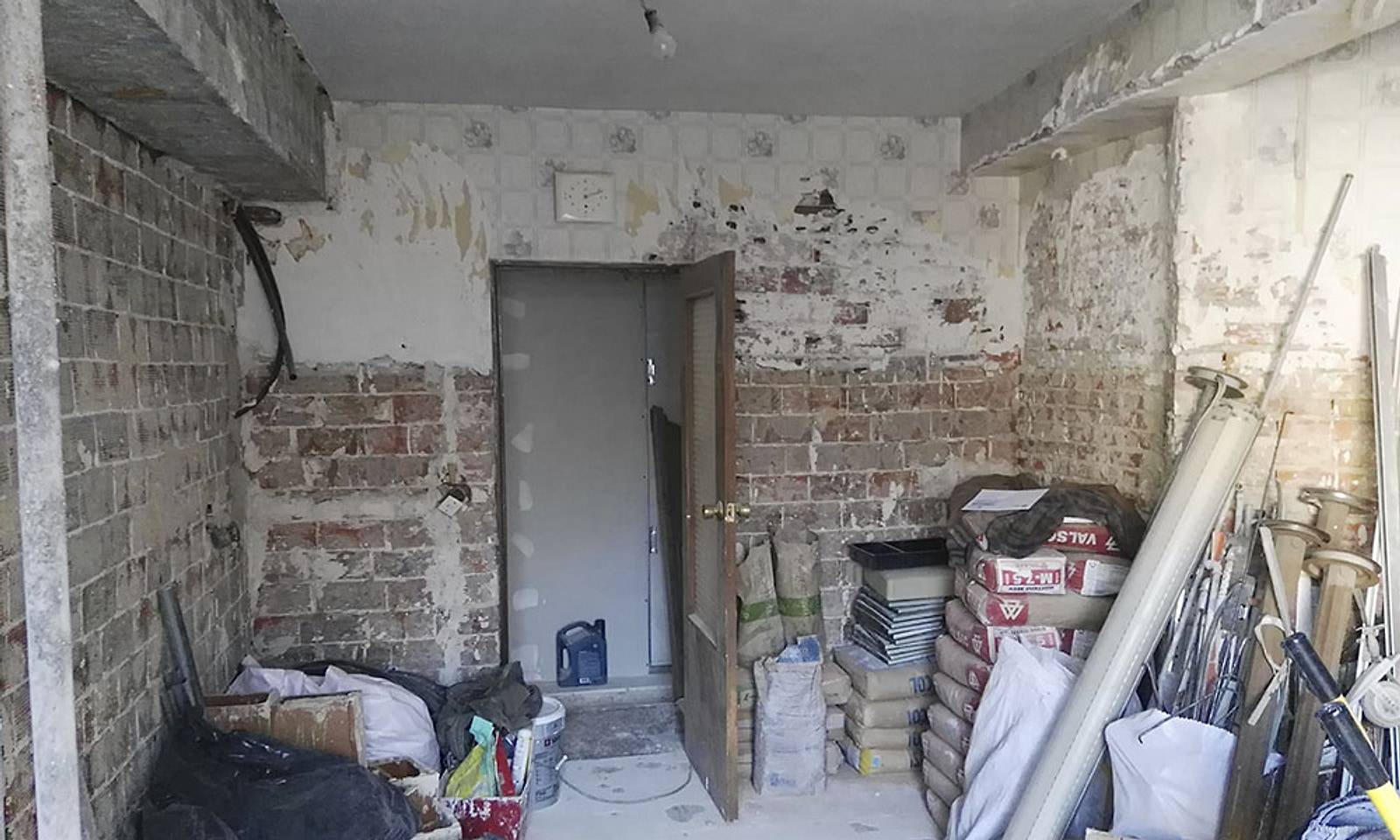 Cocina en obra con las paredes picadas, el ladrillo a la vista y material apilado