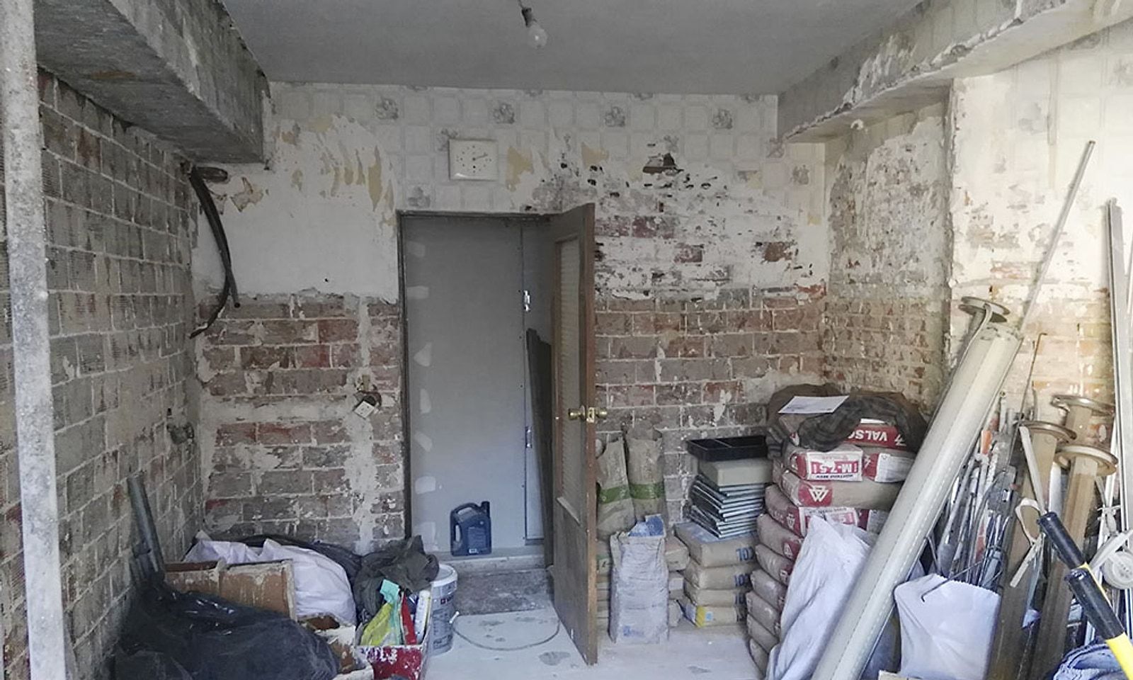 Cocina en obra con las paredes picadas, el ladrillo a la vista y material apilado