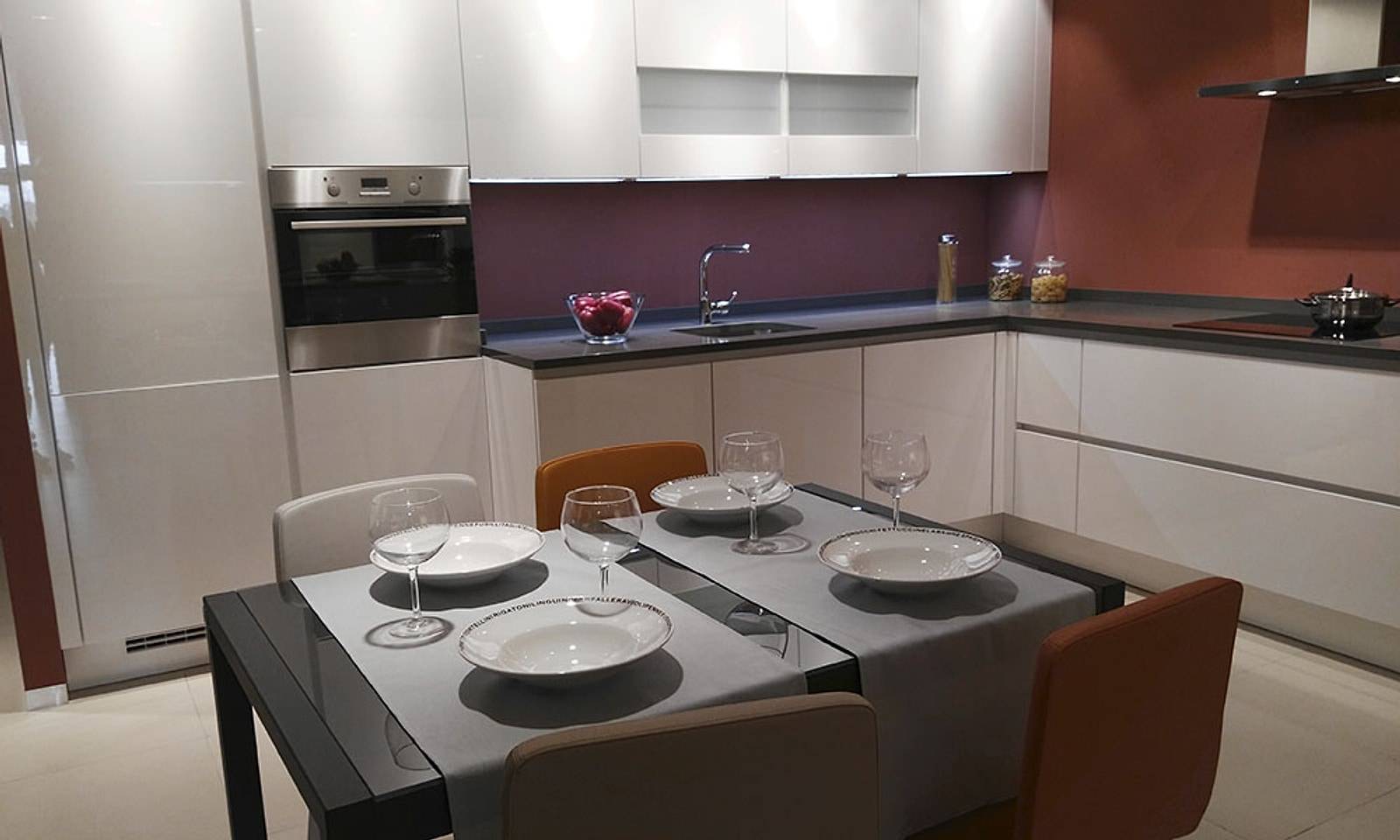 Cocina del piso reformada, con muebles blancos, pared granate, placa de inducción y mesa de comedor