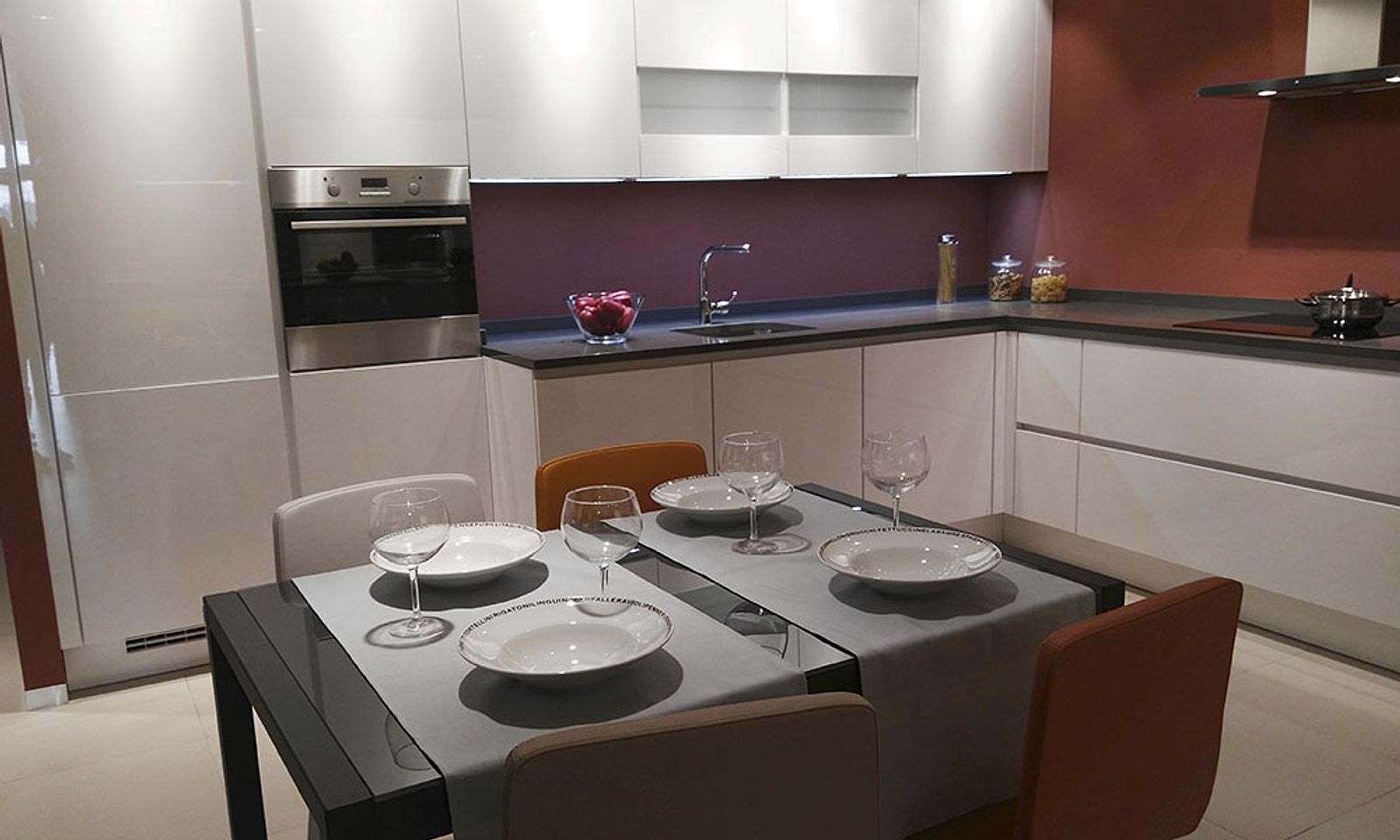 Cocina del piso reformada, con muebles blancos, pared granate, placa de inducción y mesa de comedor