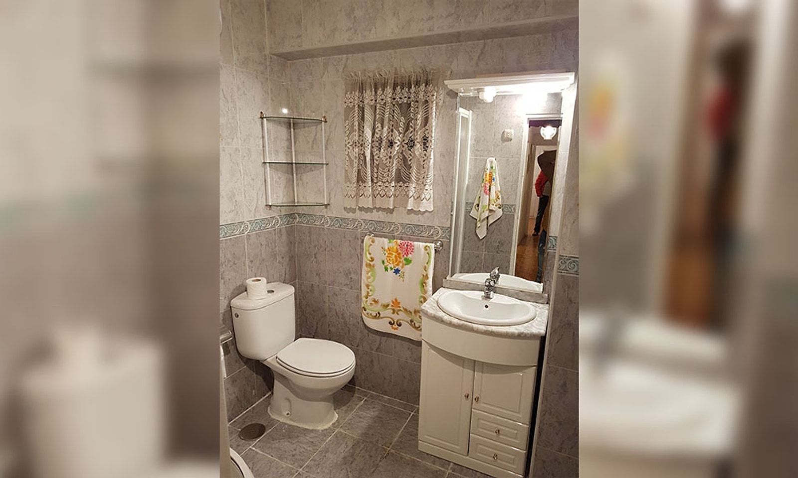 Baño antiguo con azulejo gris, lavabo con mueble blanco e inodoro