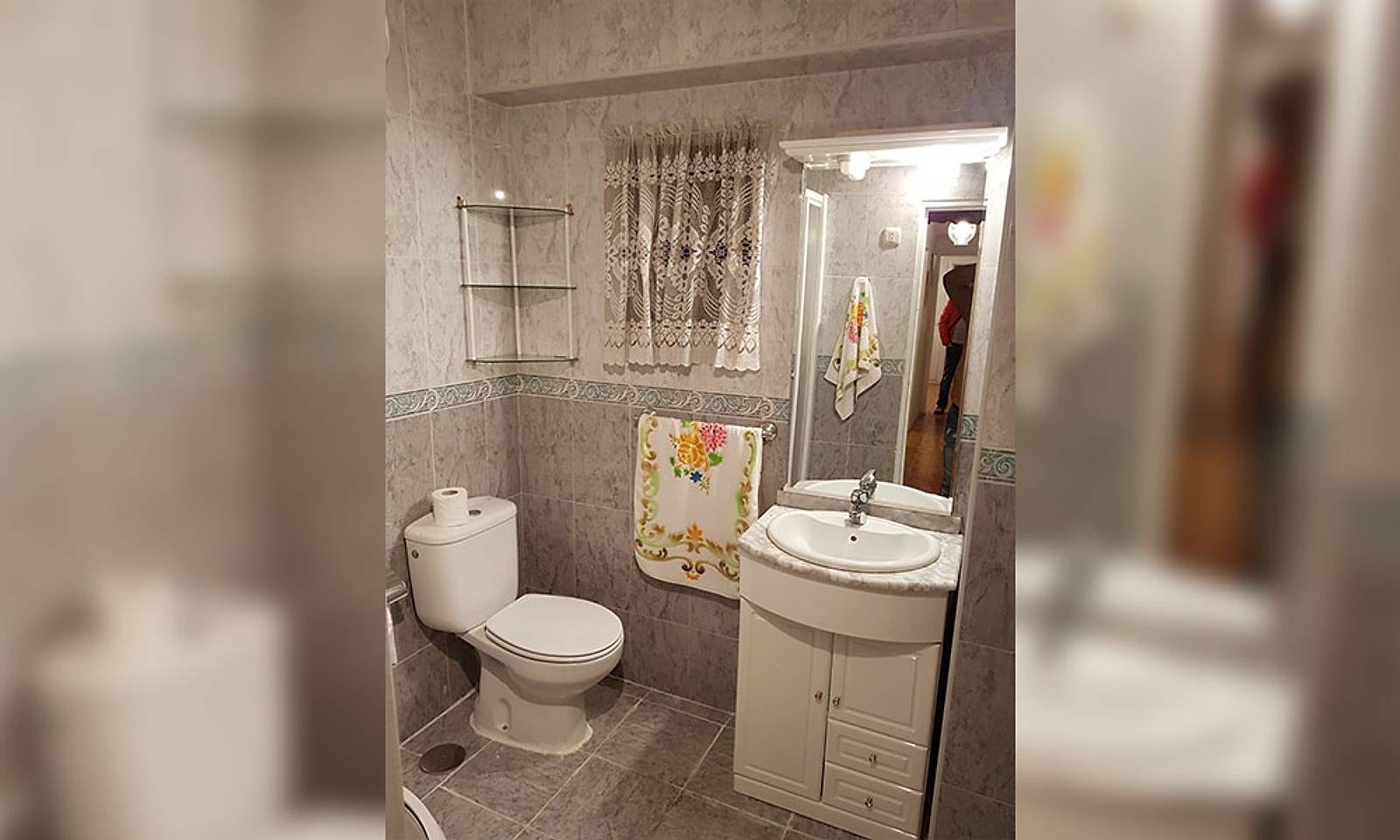 Baño antiguo con azulejo gris, lavabo con mueble blanco e inodoro