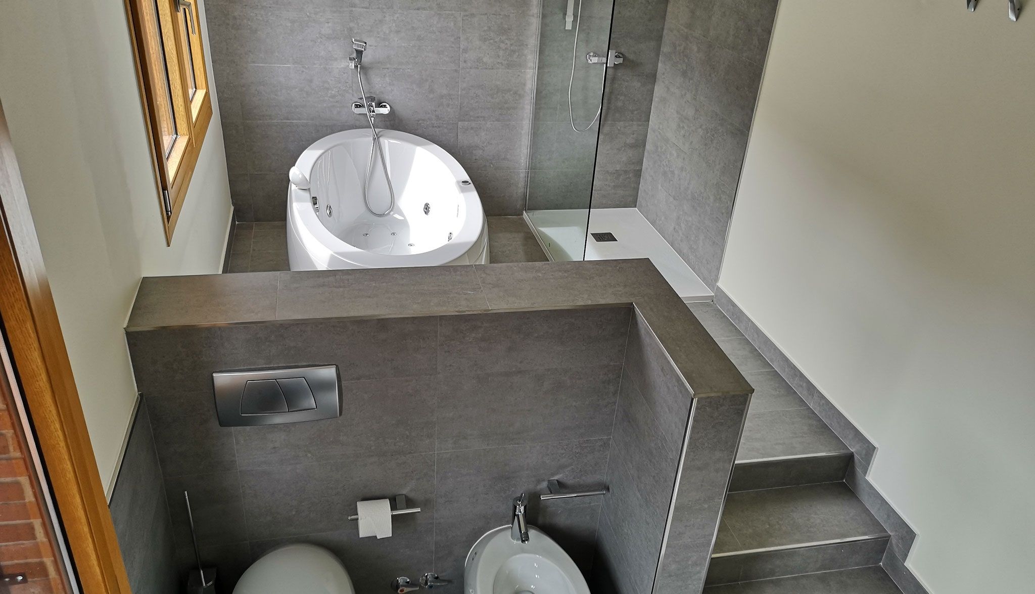 Baño con inodoro suspendido, bañera exenta y escalón revestido