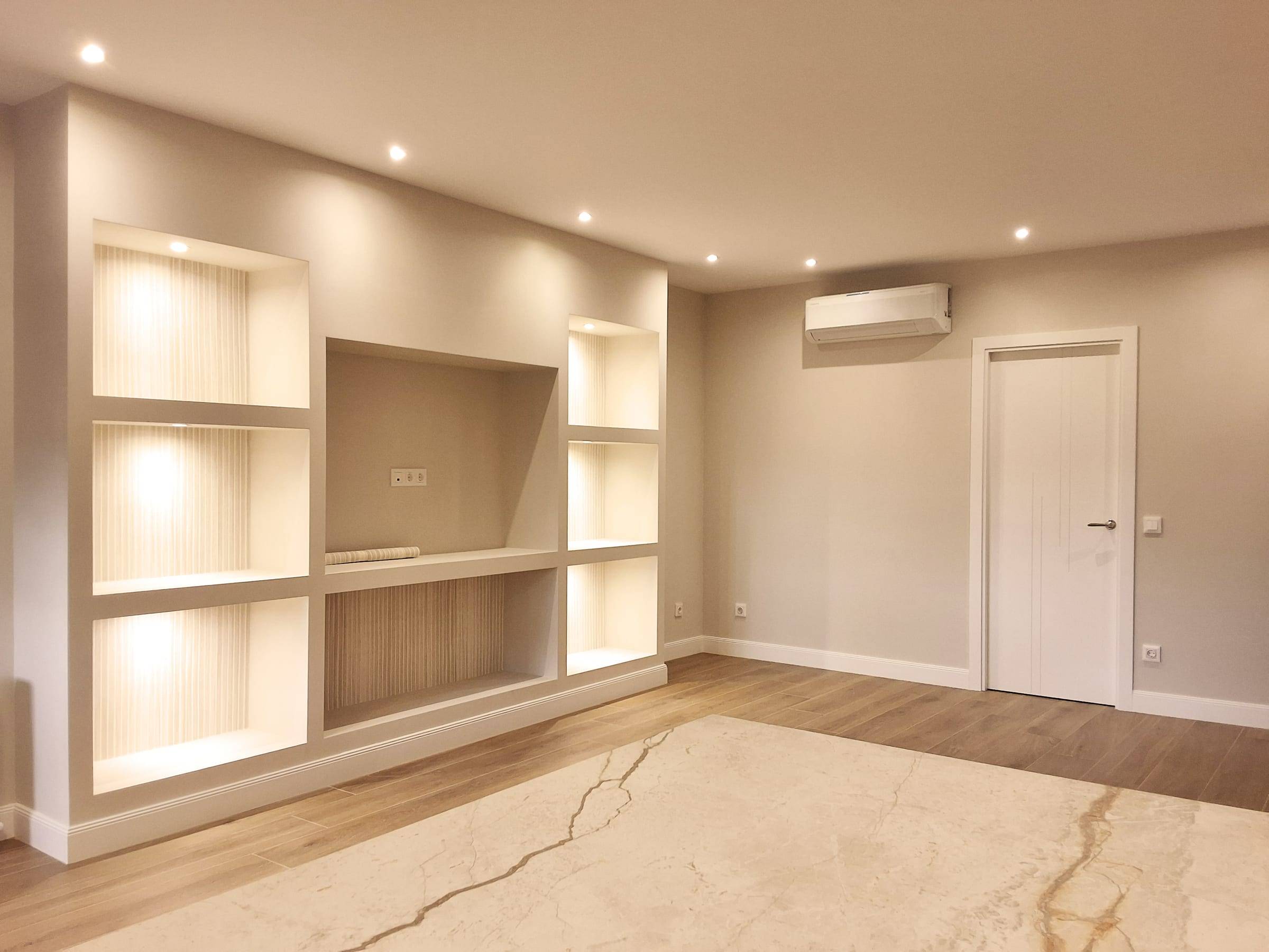 Salón reformado con estantería de obra iluminada y un split de aire acondicionado en la pared