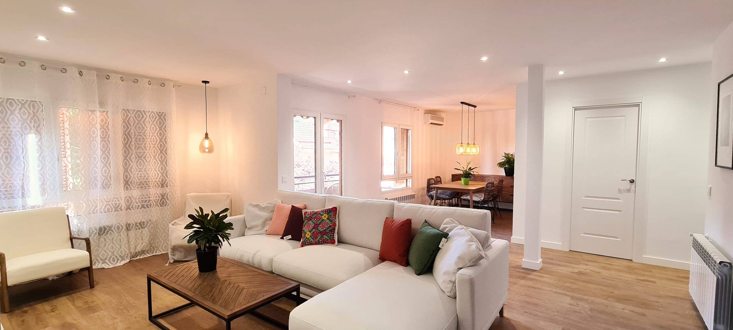Salón reformado con sofá rinconera, suelo de madera y el comedor al fondo