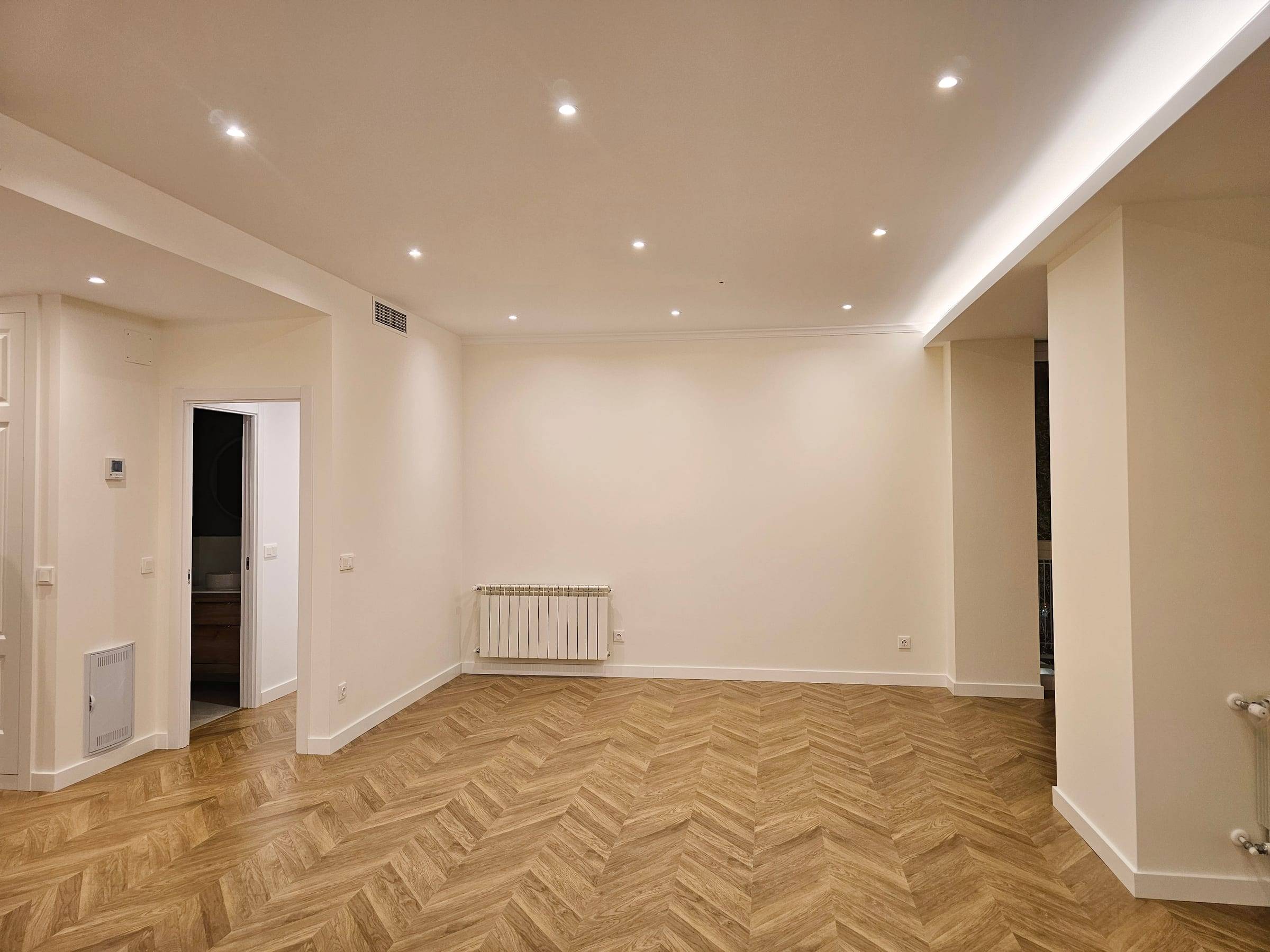 Salón reformado con suelo en espiga, luces empotradas en el techo y radiador nuevo